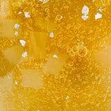 A close-up image of a yellow carbonated beverage, Silver Scoby Noel Fermented Honey by Craft & Culture - Kombucha, Kefir & Probiotics Singapore, with visible bubbles and small particles. The slightly cloudy liquid is infused with kombucha cultures, reflecting light off its surface.
