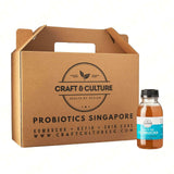 A cardboard box labeled "Craft & Culture - Kombucha, Kefir & Probiotics Singapore" sits beside a small bottle of Red Robe Da Hong Pao Black Tea Kombucha. The bottle, with a black cap and orange label, hints at its unique blend within.