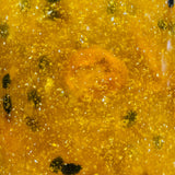 Close-up of a yellowish jelly with silver specks , passionfruit seeds and bubbles