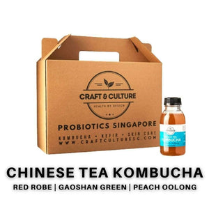A cardboard box says "Craft & Culture - Kombucha, Kefir & Probiotics Singapore," beside a bottle labeled "Chinese Tea Kombucha Series - The Specialties - Kombucha Set 2." Flavors displayed include Da Hong Pao, Gaoshan Green, and Peach Oolong.